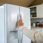 Main appuyant sur le panneau de commande d'un frigo américain Samsung